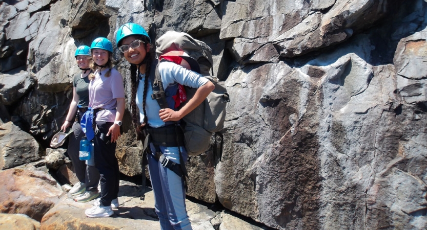 Three people wearing safety gear smile for the photo near a rock wall.